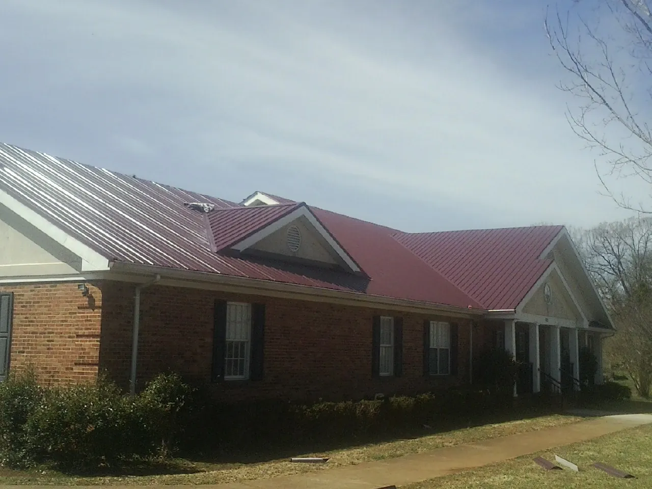 Red metal roof with gabled entries on a long brick building, from a Hail Damage Roof Repair job in Bladensburg