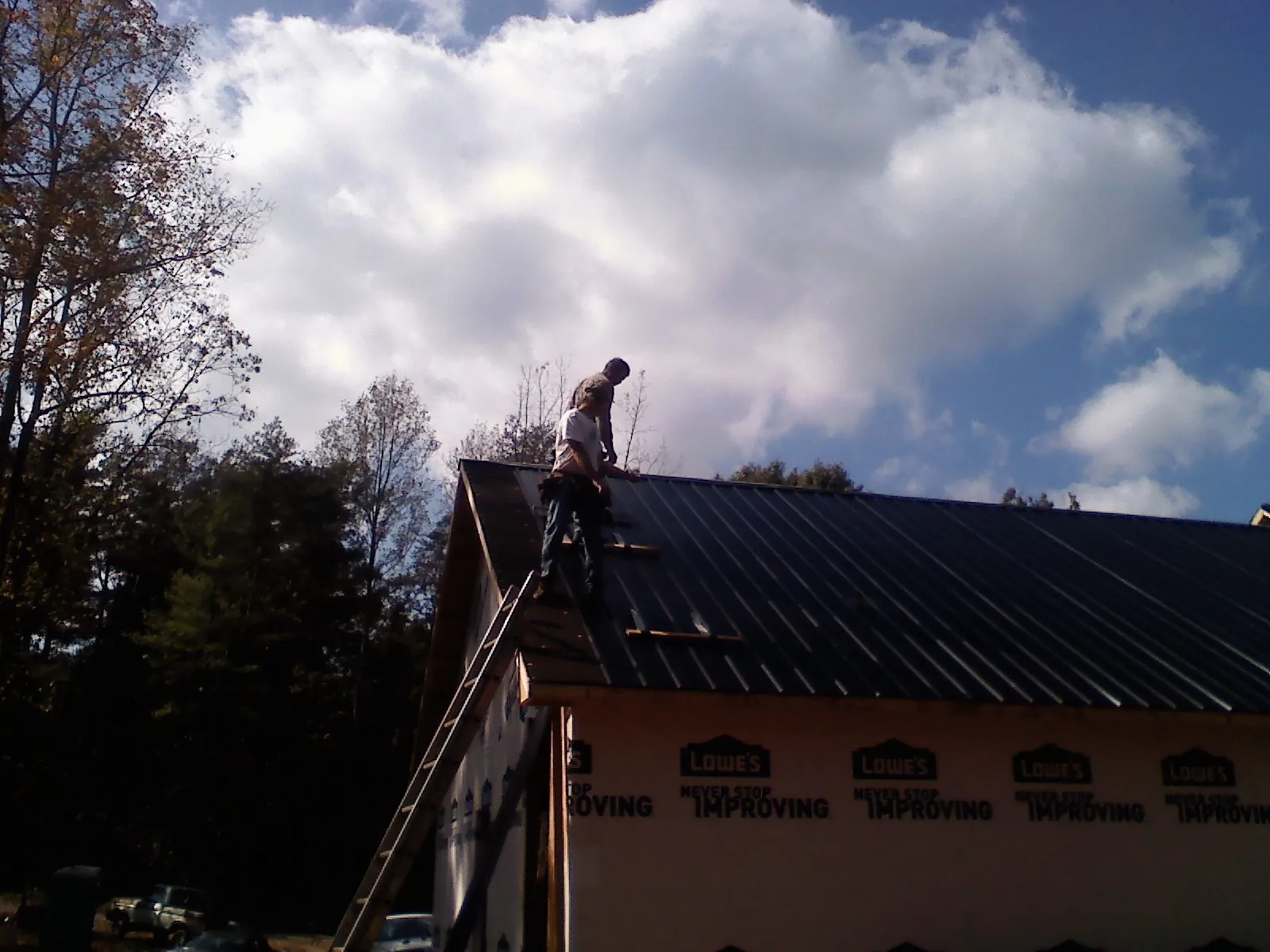 Roofer fastening dark metal panels high against a cloudy sky, from a Roof Inspection job in Bladensburg