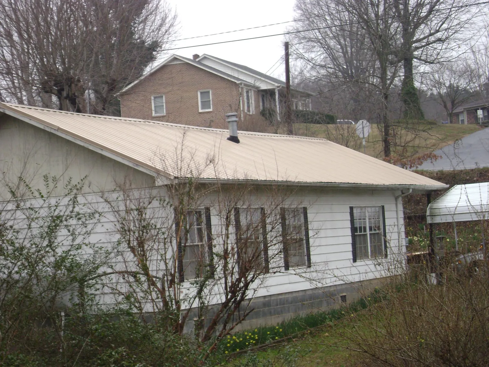 Tan metal roof on a white sided house set into a hillside — Commercial Roofing by Roofing Brothers in Bladensburg